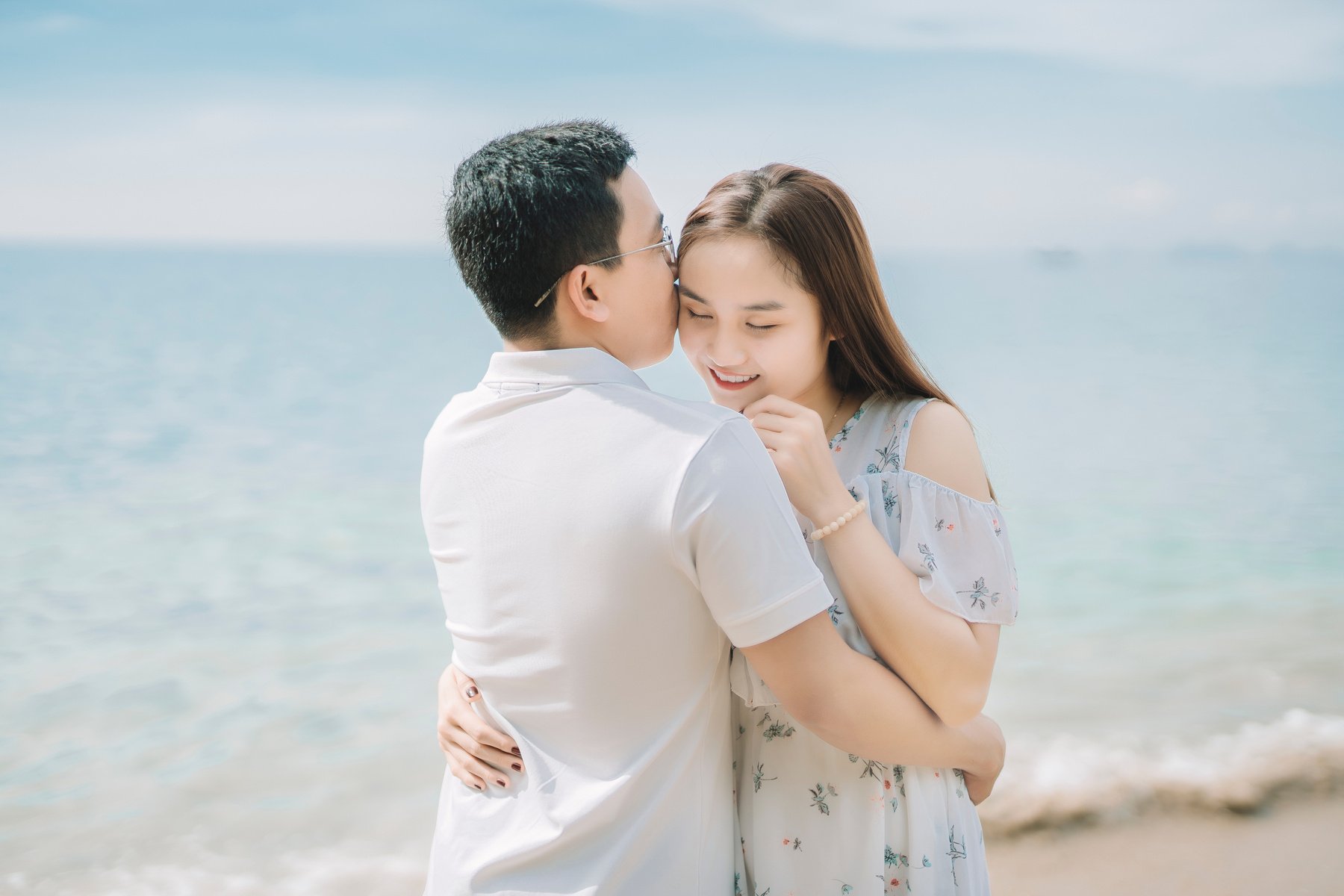 Asian couple hugging on beach near sea